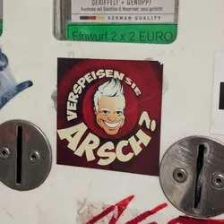 A sticker on a vending machine titled "Verspeisen sie Arsch?"