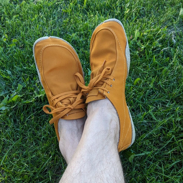 My feet in a pair of brown barefoot shoes, laying on grass