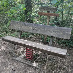 A bench standing on a large spring, with a sign above it saying "Use at your own risk"