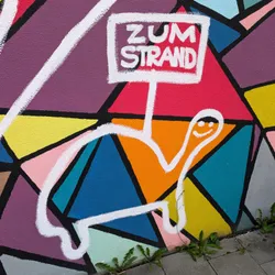 Graffiti on a wall with lots of colorful triangles and a small turtle with a sign that says "Zum Strand" which translates to "To the beach"